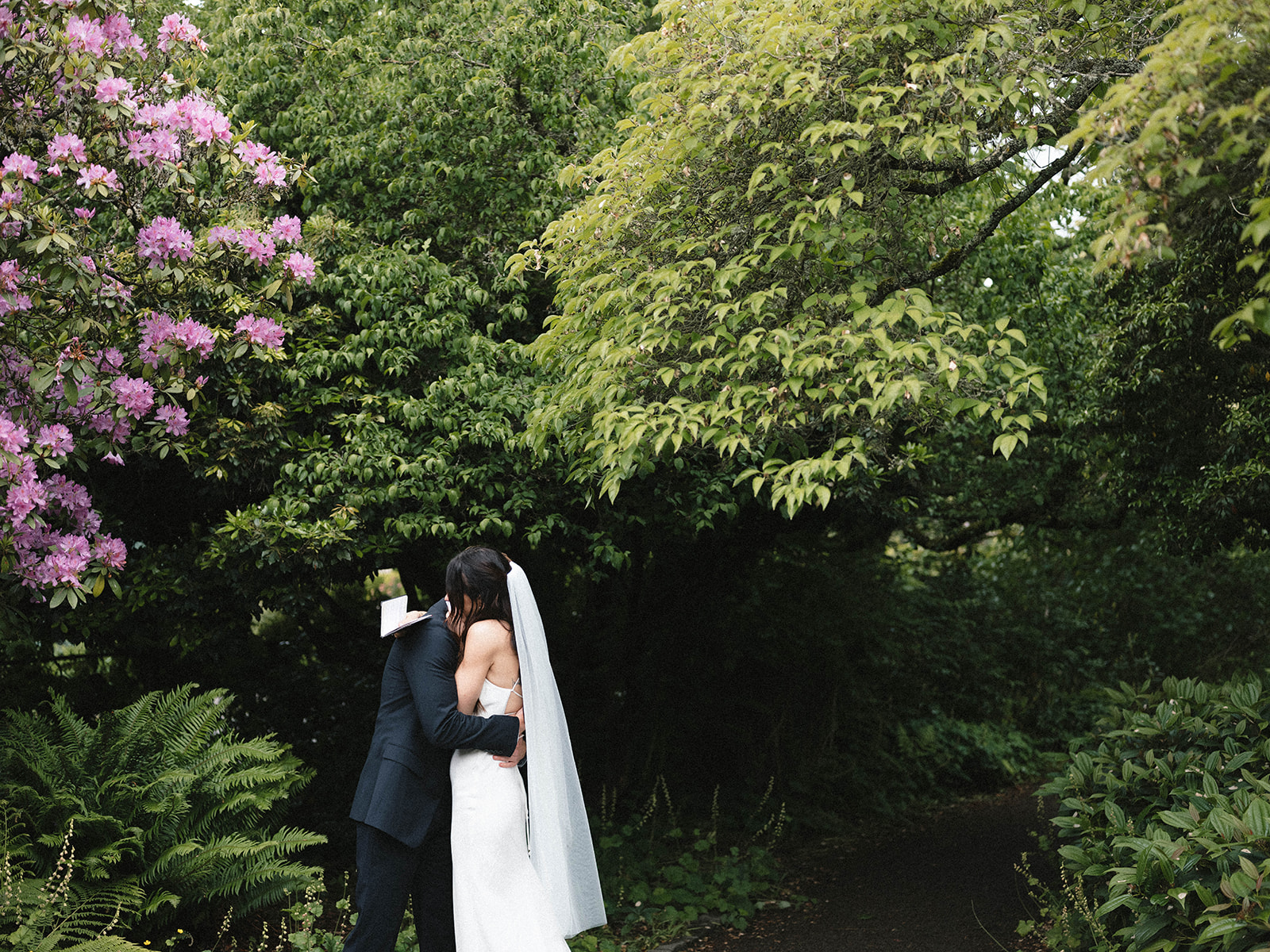 Couple embracing after exchanging vows, surrounded by vibrant greenery and pink blossoms at Parsons Gardens.