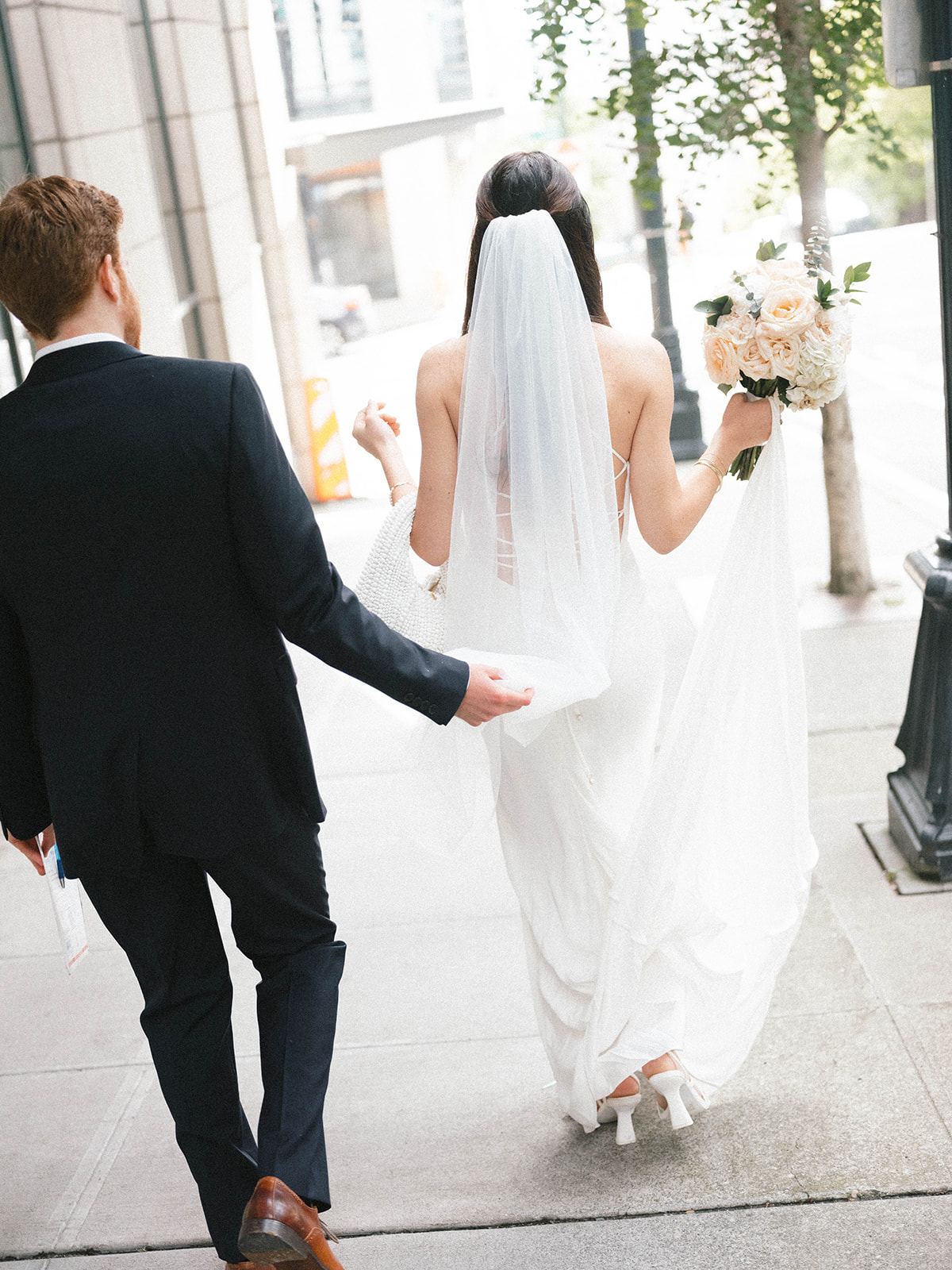 Bride and groom walking through downtown Seattle, the groom gently holding the bride’s veil as they walk to the courthouse.