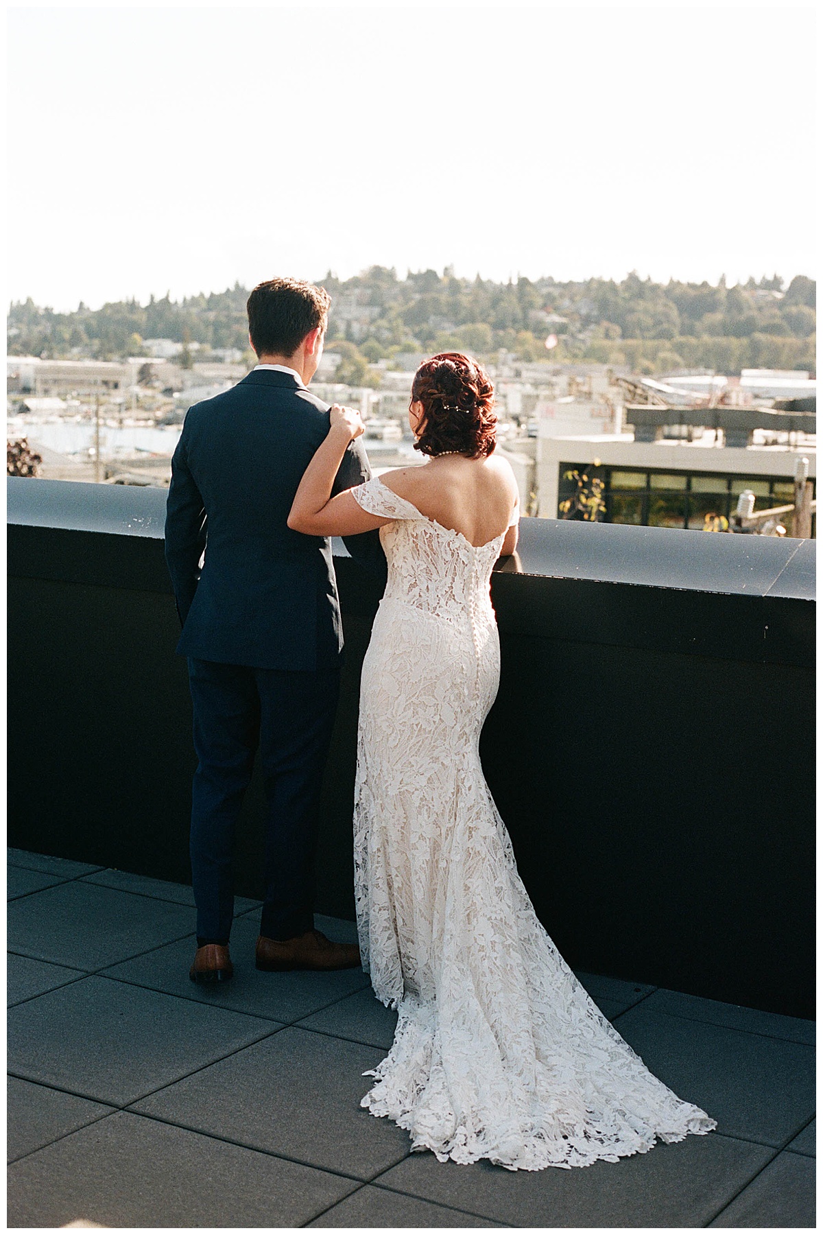 Couple standing on the Olympic Rooftop Pavilion terrace, overlooking the Ballard cityscape in the afternoon sunlight.