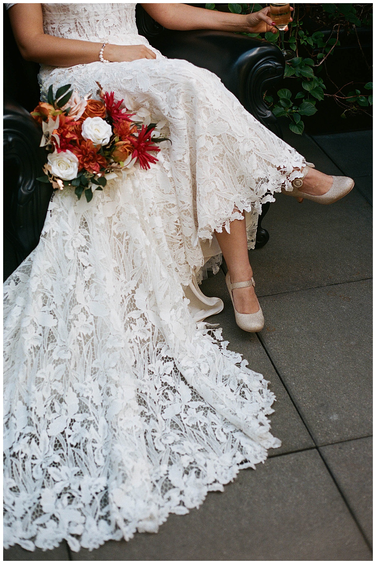 Bride’s intricate lace gown and vibrant bouquet with champagne glass in hand, styled for a fall wedding.