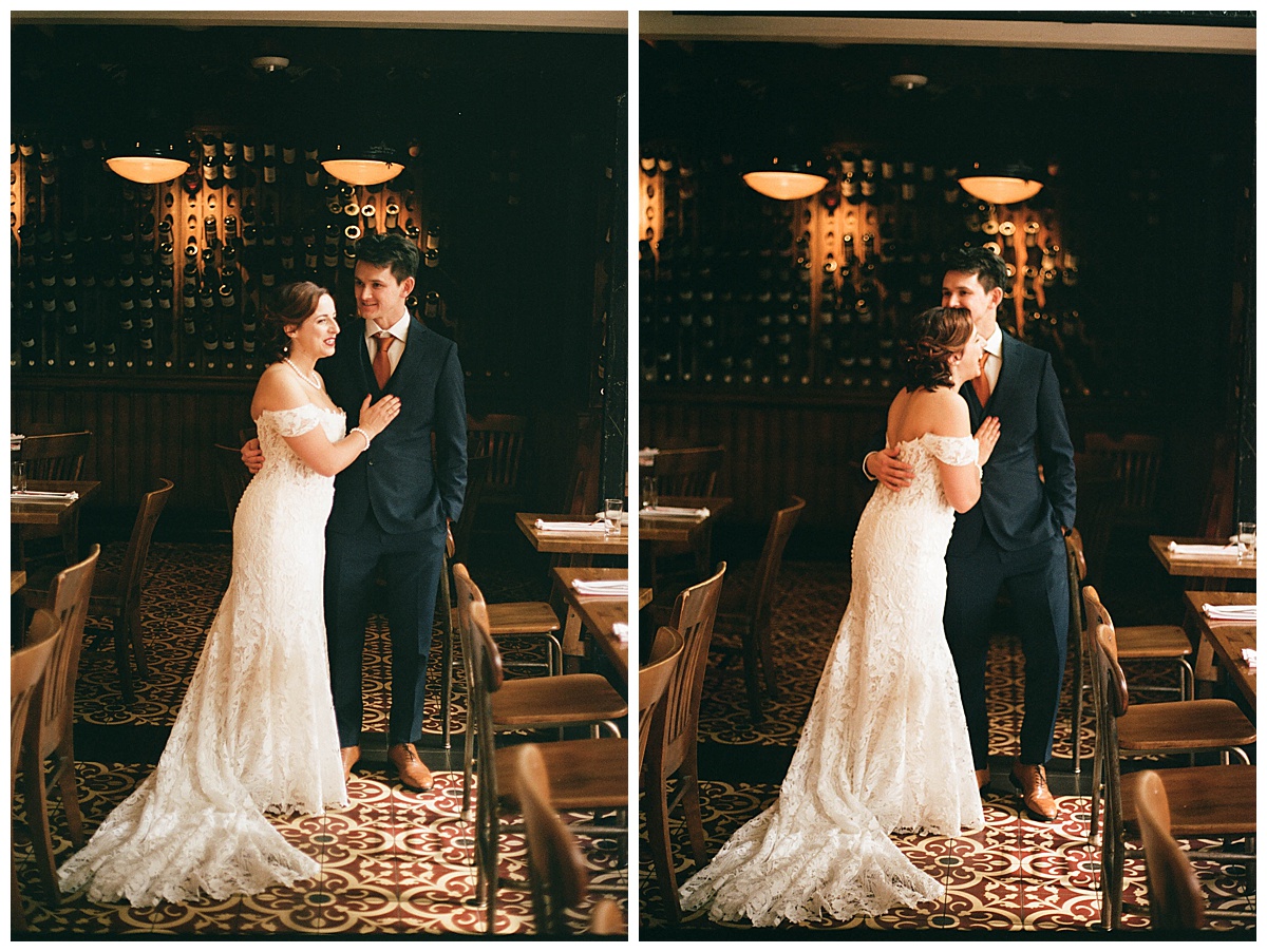 Bride and groom standing in a warm wine room interior with walls lined with bottles and cozy lighting.