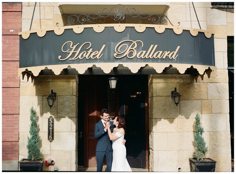 Bride and groom smiling and embracing under the historic Hotel Ballard sign, a charming urban touch.