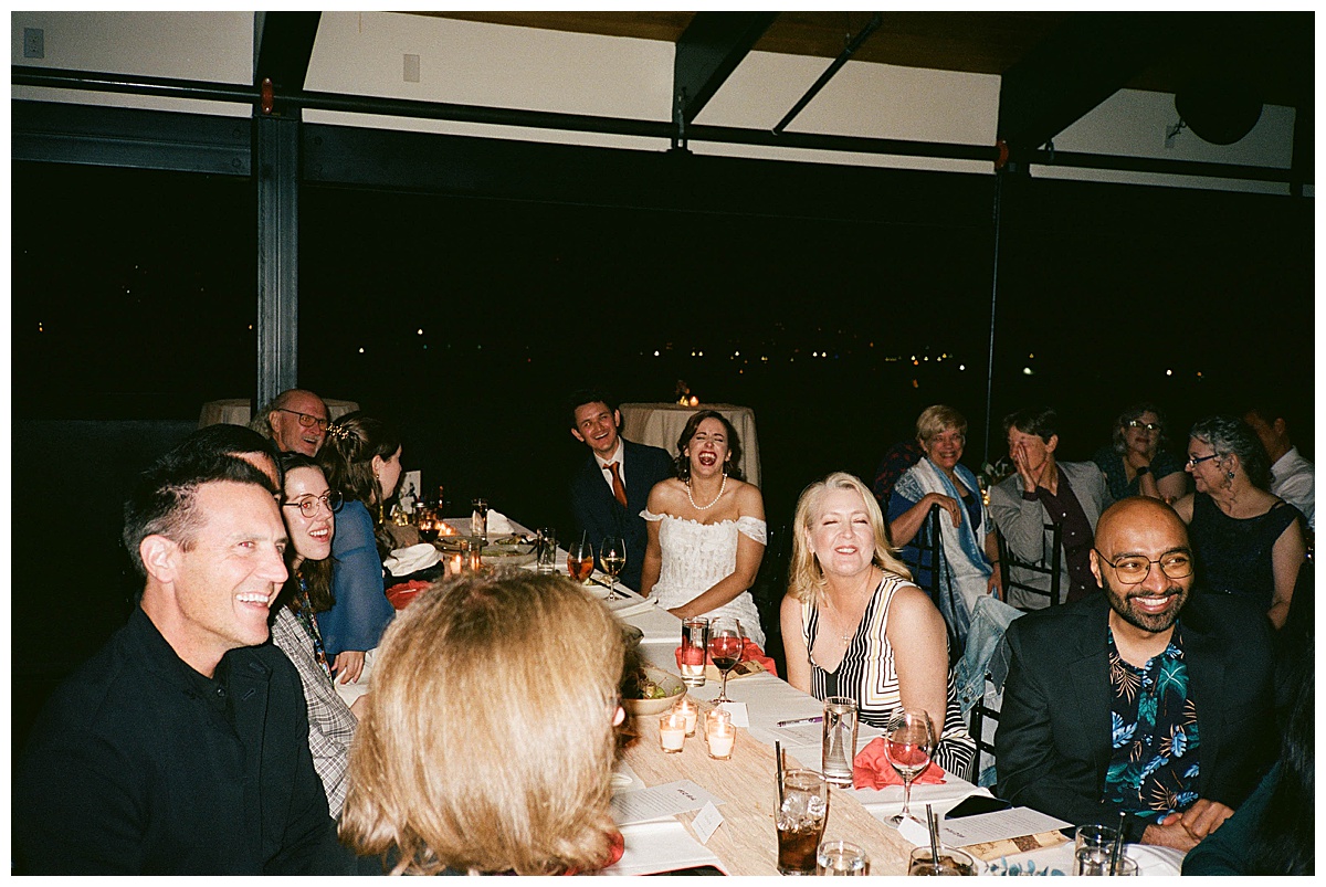 Bride and groom enjoying laughter with their guests at the head table during the wedding reception.