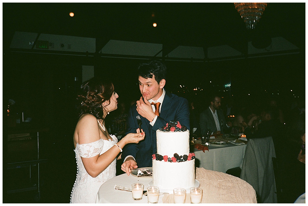 Bride and groom cutting their cake with berries, sharing playful expressions during their wedding reception.